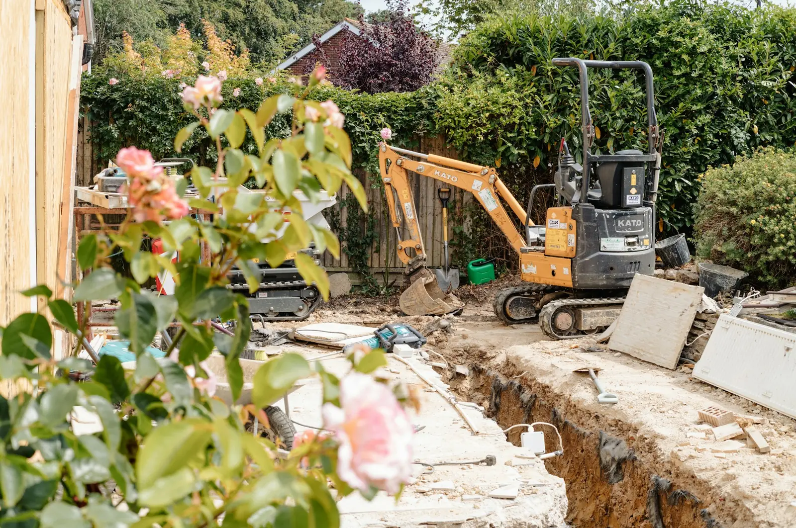 Minigrävare bredvid ett nygrävt schakt i en villaträdgård, rosor i förgrunden